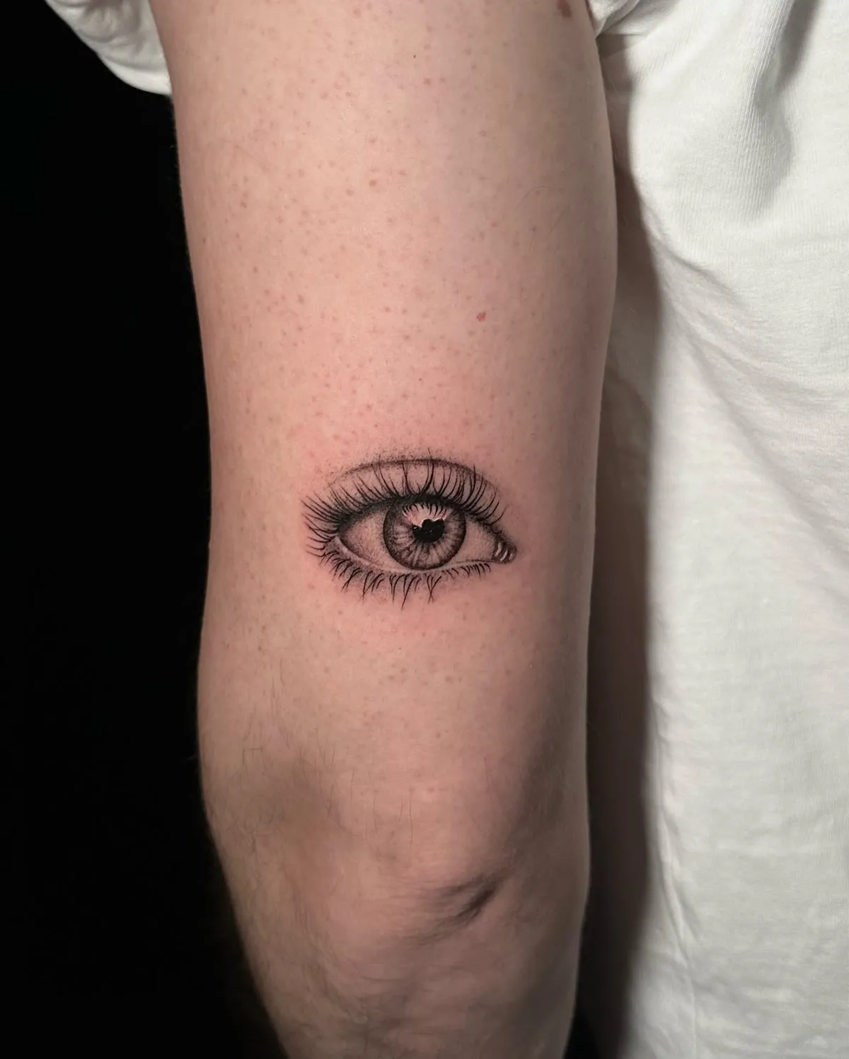 A single eye in soft grey shading on the back of an arm.