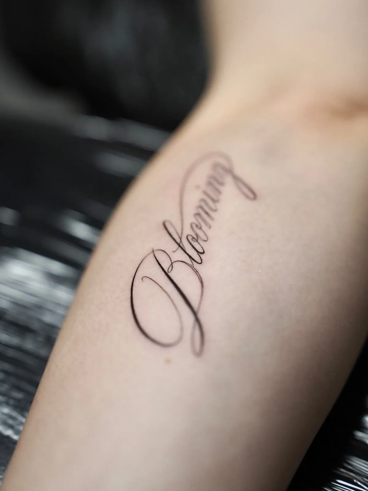 The word Blooming in tall fine script, running down the inside of a forearm.