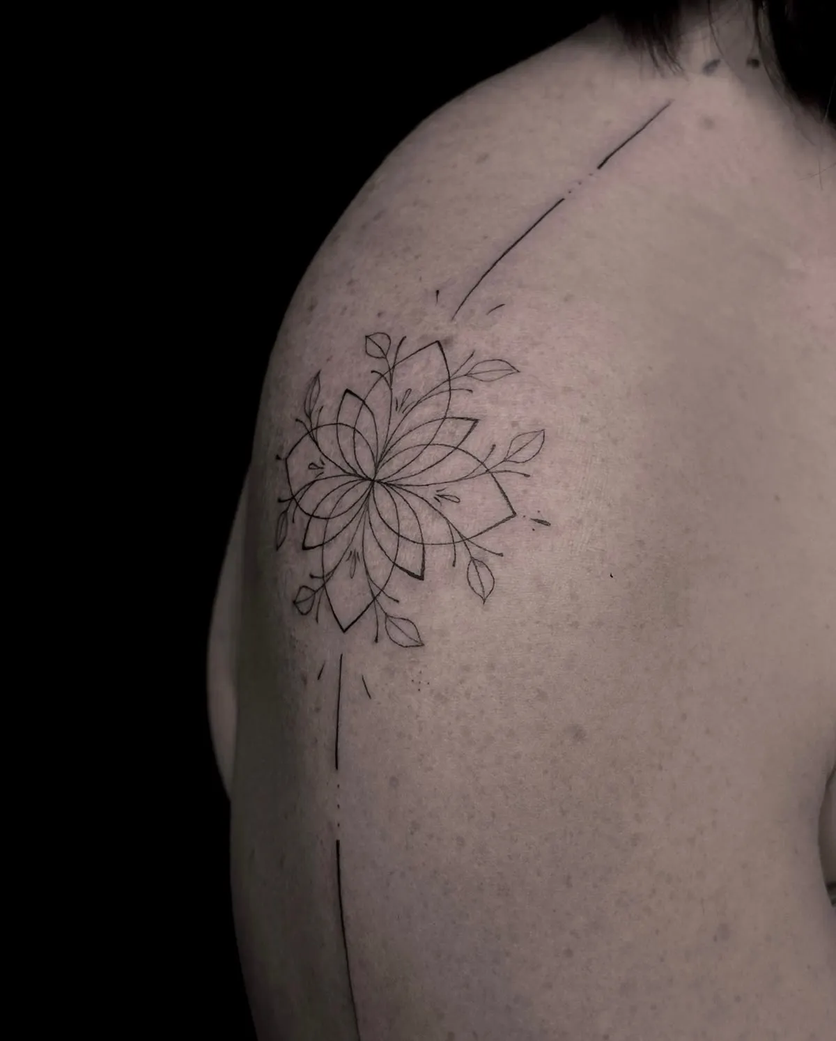 An ornamental flower in thin lines, spread across a shoulder blade.