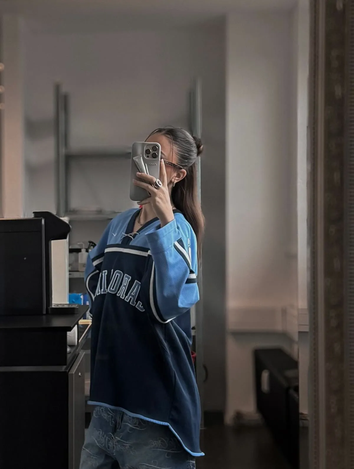 A tattoo artist photographed in a studio mirror, machine and worktop behind.